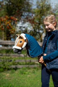 Girl holding the golden Hobby Horse dressed in a petrol blue blanket and white fur halter, autumn berries behind