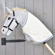 The Hobby Horse LarDen Blanket Cream Pearl is a plush hobby horse with a grey head, black bridle, and a cream pearl blanket with blue trim on a wooden stick, displayed against a grey wooden wall.