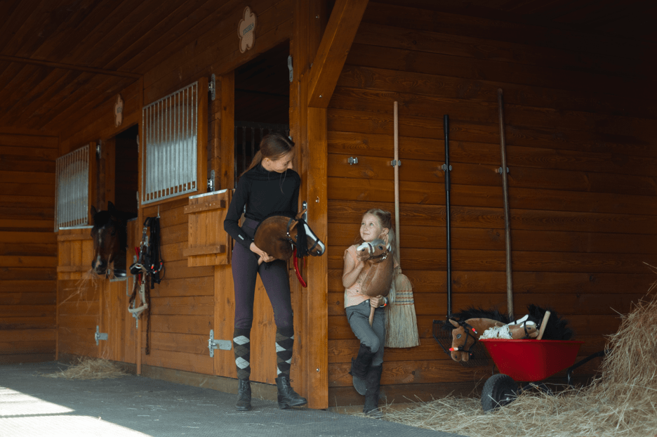 Unge med kæpheste uden for en rideklubs stalde af træ