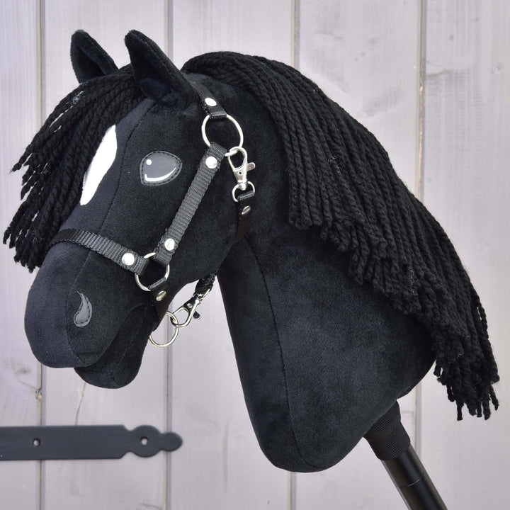 Sort Hobby Horse kæphest i plys med en hvid plet i hovedet, sort manke af garn og trense foran en lys træbaggrund