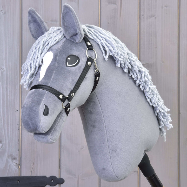 Grå Hobby Horse kæphest med en hvid plet i panden, sort trense og manke af garn foran en træbaggrund