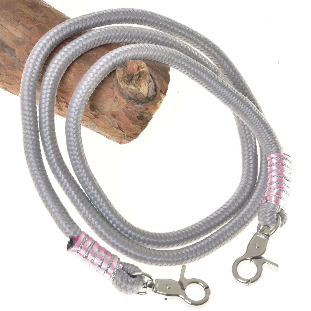 The Reins Tizian by Hobby Horse LarDen feature coiled gray polypropylene with silver lobster clasps and pink-silver wraps at each end, shown on wood against a white background—ideal as stylish handmade or hobby horse reins.
