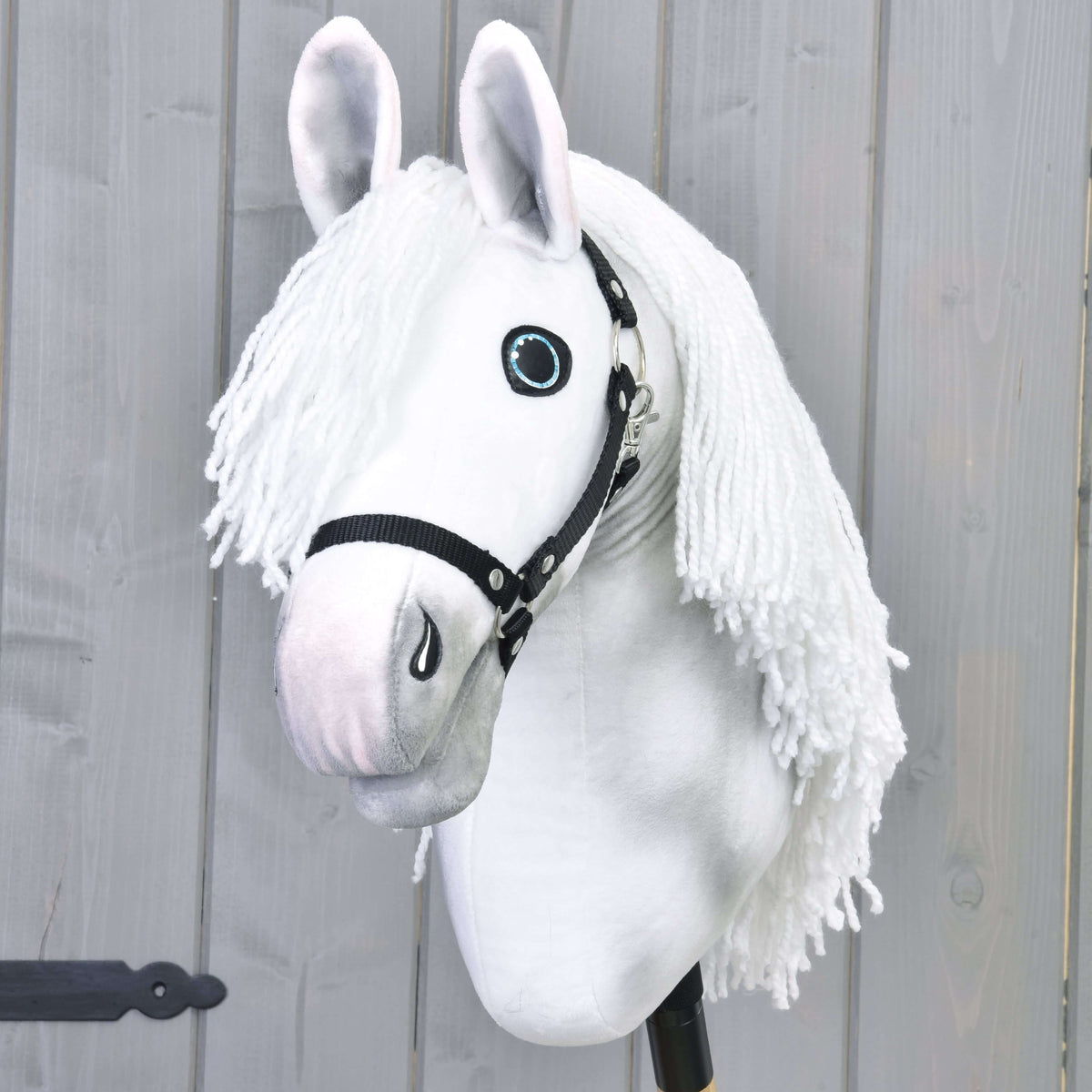 The Hobby Horse LarDen Elektra features a hand-painted white mare with a long yarn mane, blue eyes, and black halter, mounted on a stick and shown against a light gray wooden wall.