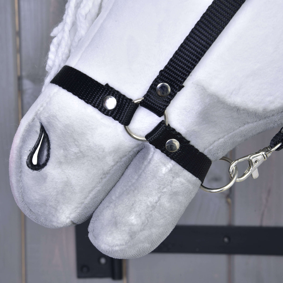 Close-up of the Hobby Horse LarDen Elektra with Black Halter, showing its plush white face, black fabric halter with silver rings and clip, black-stitched nostril, set against a wooden background.