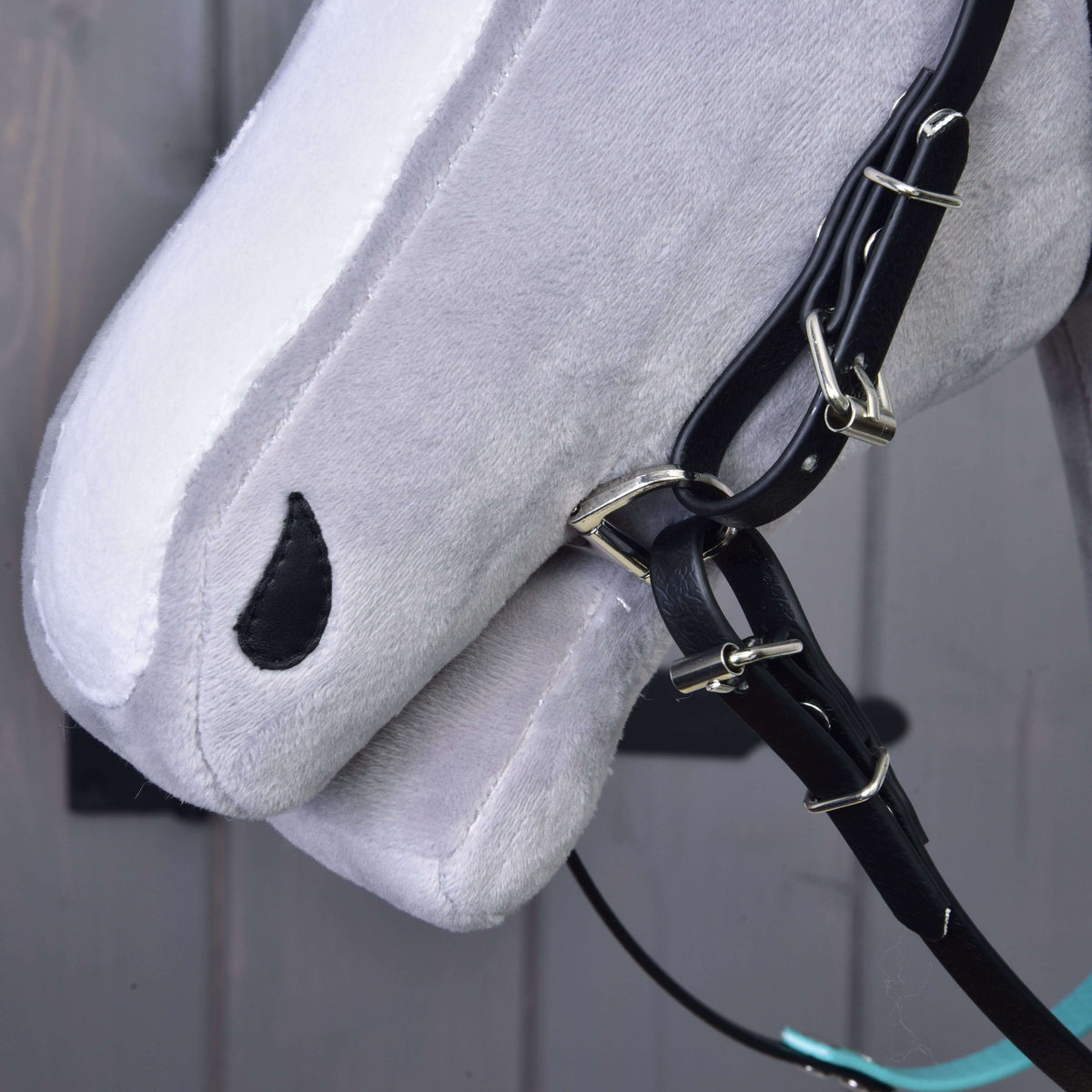 Close-up of the muzzle of a grey Hobby Horse with the black cheek straps, buckles and bit ring, no noseband