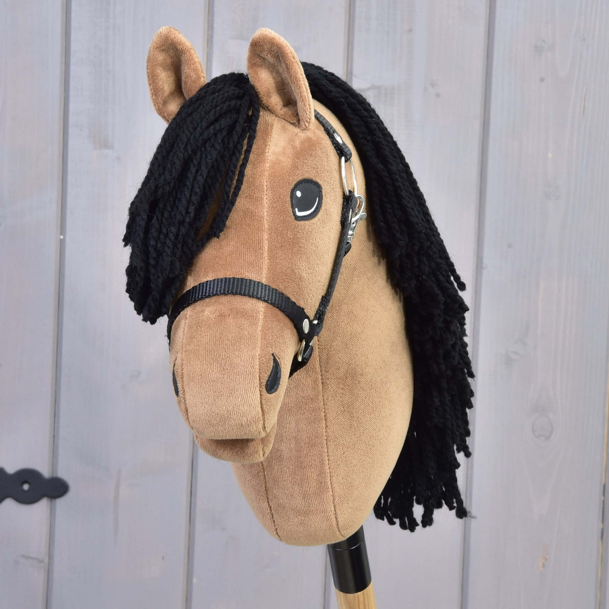 The Hobby Horse LarDen "Hobby Horse Samantha with Black Halter" features a tan plush head, black yarn mane, black halter, button eyes, and is mounted on a wooden stick—styled as an English Thoroughbred.