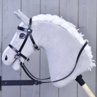 A close-up of a gray plush hobby horse with a white mane on a wooden stick, featuring Hobby Horse LarDen's complete black bridle from leatherette, set against a light wooden panel background.
