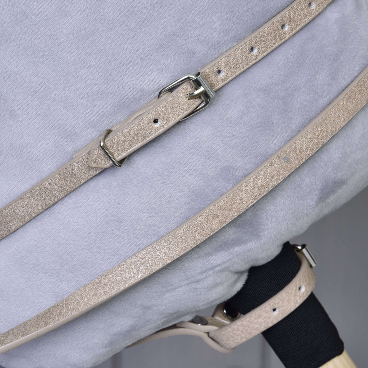 A close-up of beige Bordeaux leatherette straps with metal buckles from the Hobby Horse LarDen bridle, reins, and martingale set, fastened over a soft light gray plush surface.