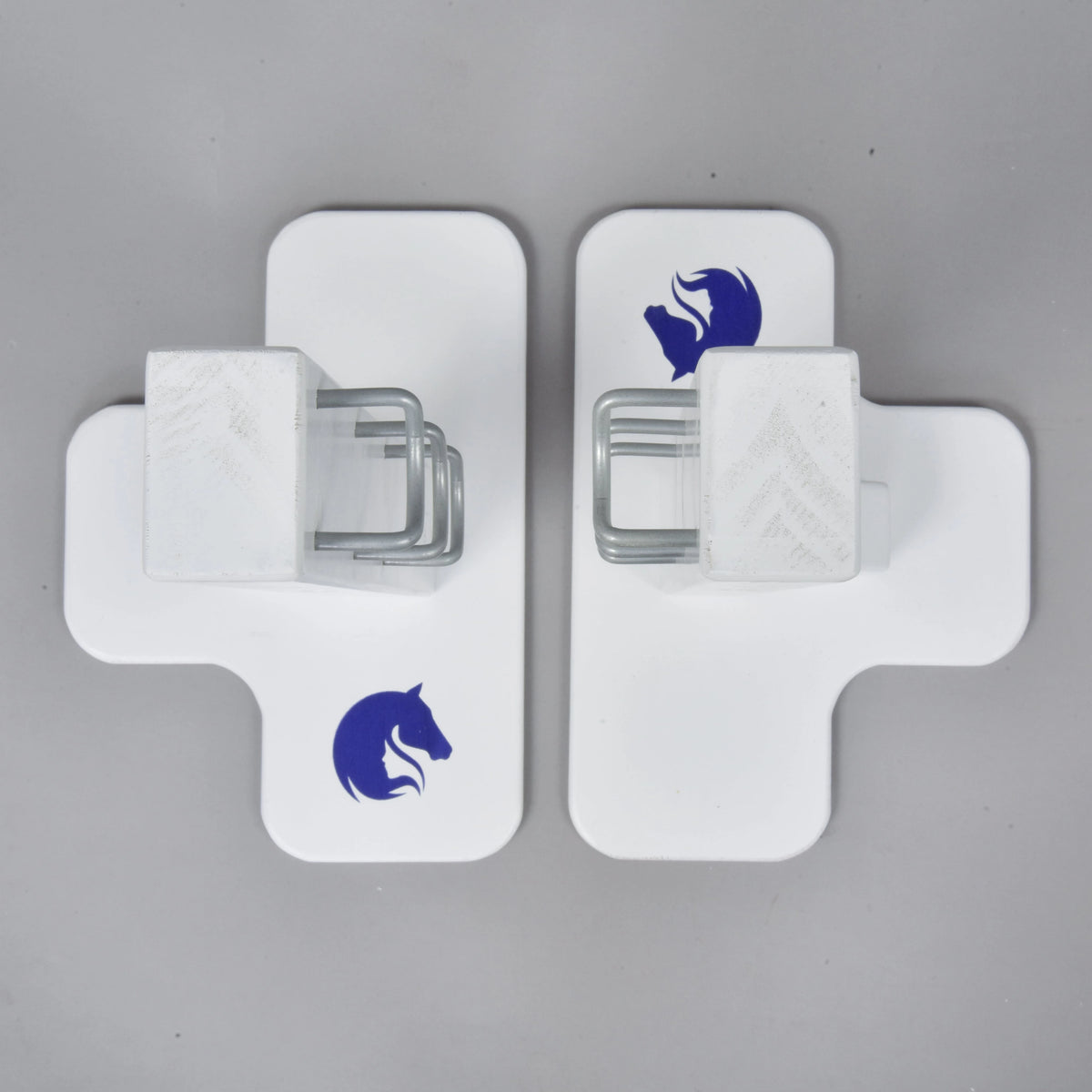 Two white cross-shaped Jump 50 cm / 20 inch obstacles by Hobby Horse LarDen, each with a blue horse head logo and central metal bracket, face each other on a gray surface—ideal for adjustable height hobby horsing jumps indoors or outdoors.
