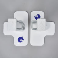Two white cross-shaped Jump 50 cm / 20 inch obstacles by Hobby Horse LarDen, each with a blue horse head logo and central metal bracket, face each other on a gray surface—ideal for adjustable height hobby horsing jumps indoors or outdoors.