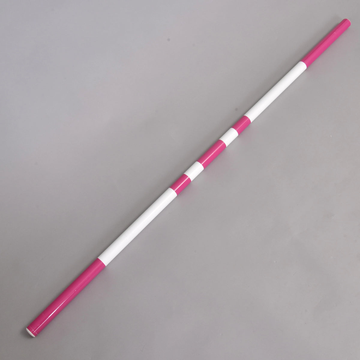 The Hobby Horse LarDen Jump pole pink, featuring alternating pink and white segments, is displayed diagonally on a plain gray surface.