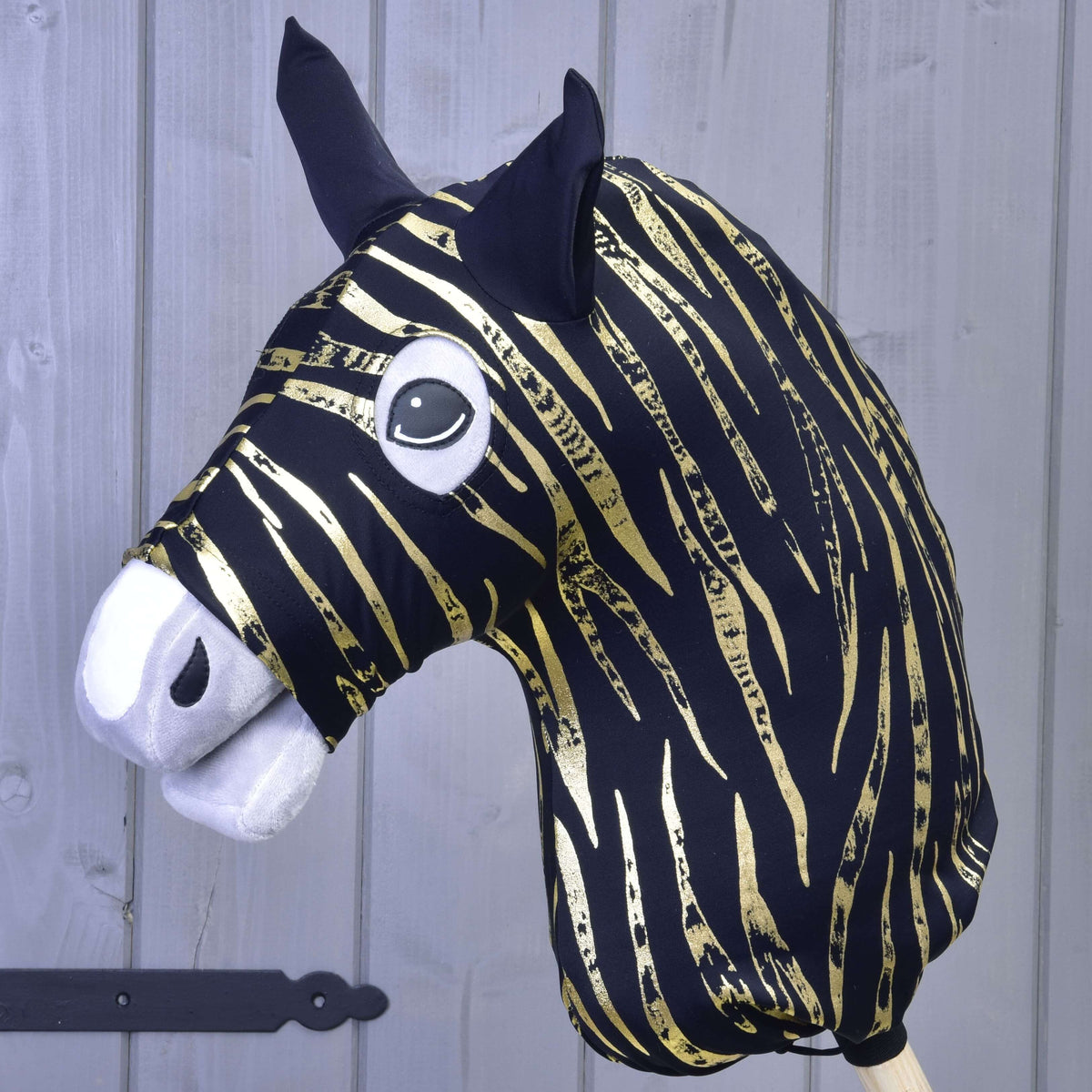 The Hobby Horse LarDen protective suit Zebra Gold (Lycra) features a black and gold zebra-striped head, black ears, white felt snout, and large cartoon eyes, shown in front of a light gray wooden wall.