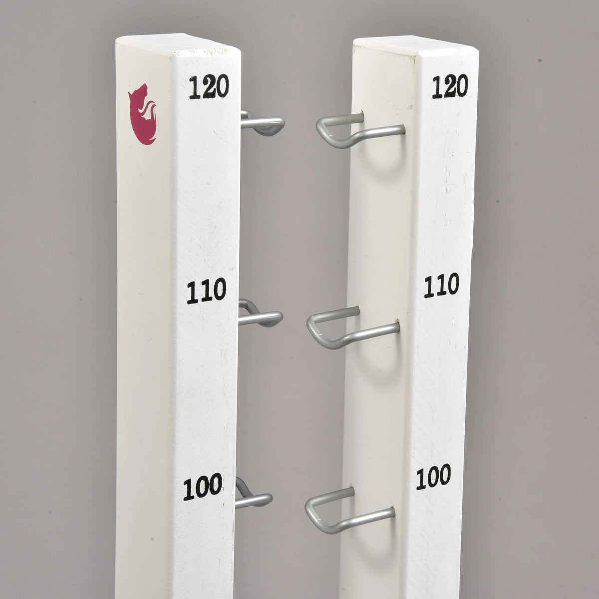 The Jump set for Hobby Horsing by Hobby Horse LarDen features two white vertical posts with metal brackets at 100, 110, and 120 heights, ideal for jumps or cavaletti. The left post is topped with a red fox logo. Background is plain gray.
