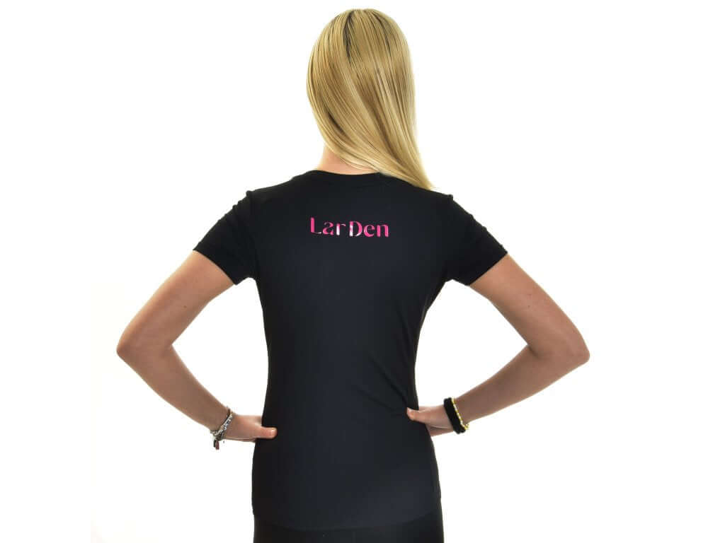 A person with long blonde hair stands facing away, hands on hips, wearing the Hobby Horse LarDen T-Shirt LarDen Active Black against a white background, highlighting the sleek Spandex fabric and “LarDen” in pink on the upper back.