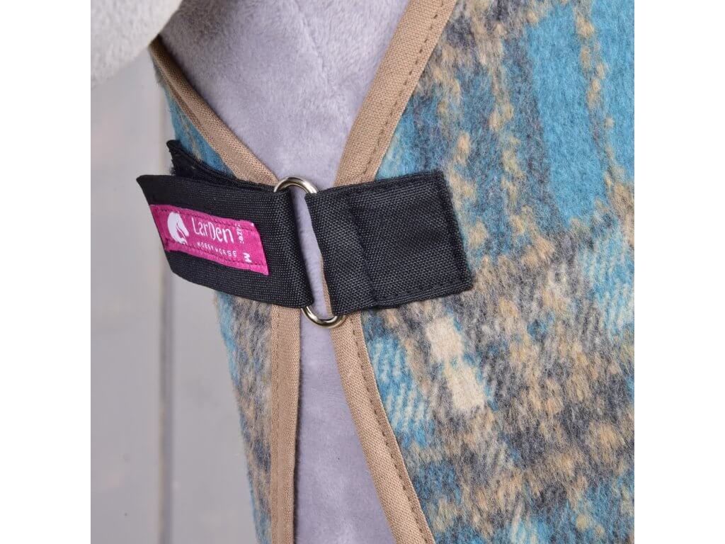 Close-up of the Stable Blanket Scottish Cube by Hobby Horse LarDen, featuring blue, brown, and gray patterns with beige trim. Secured by a black strap with a silver ring and finished with a pink label bearing the horse logo.