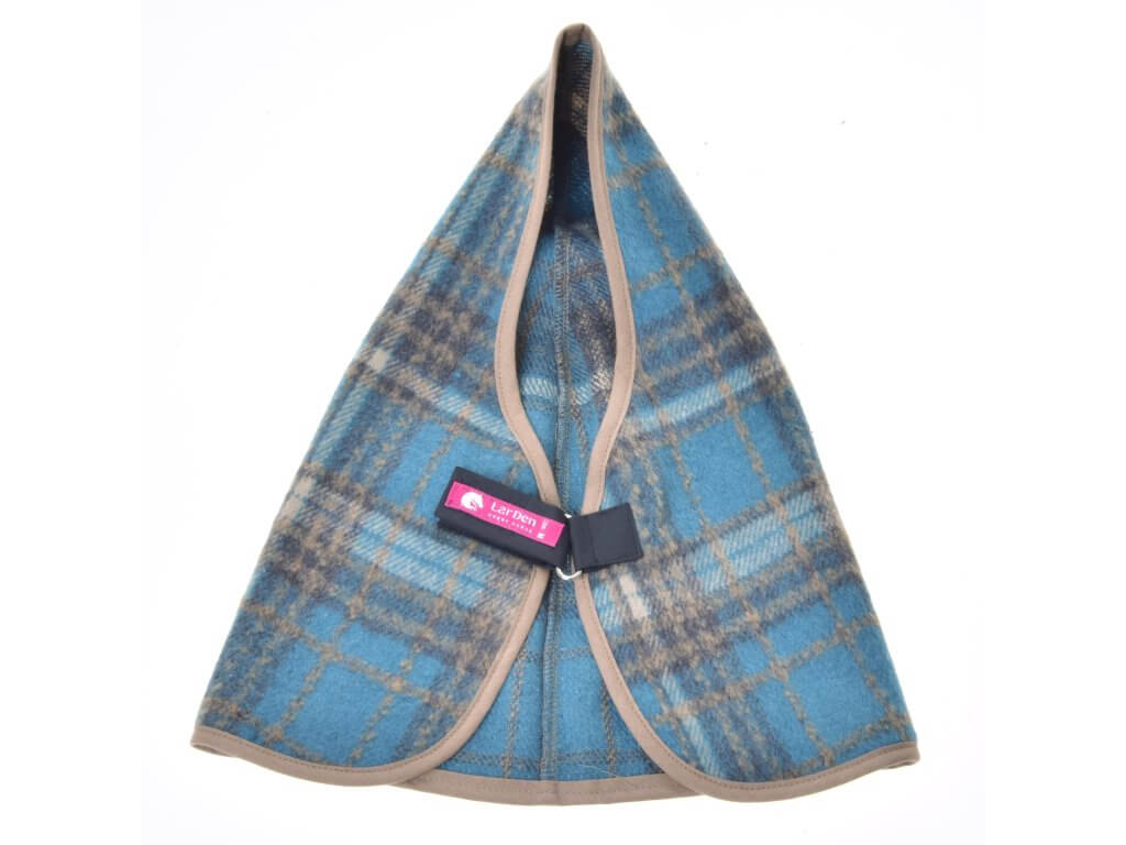 The Hobby Horse LarDen Stable Blanket Scottish Cube is a blue and beige plaid wool dog coat with beige trim, folded in a triangle. It features a black strap with a pink label and Velcro closure across the middle.
