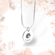 A Hobby Horse LarDen necklace with a round pendant featuring a horse head and the word "Leiden," crafted from surgical stainless steel, displayed against soft pink and white holiday decorations.