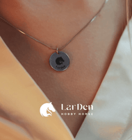 A close-up shows a person wearing the Hobby Horse LarDen necklace with a round hobby horse pendant made of surgical stainless steel, featuring the LarDen logo—perfect for hobby horsing fans.