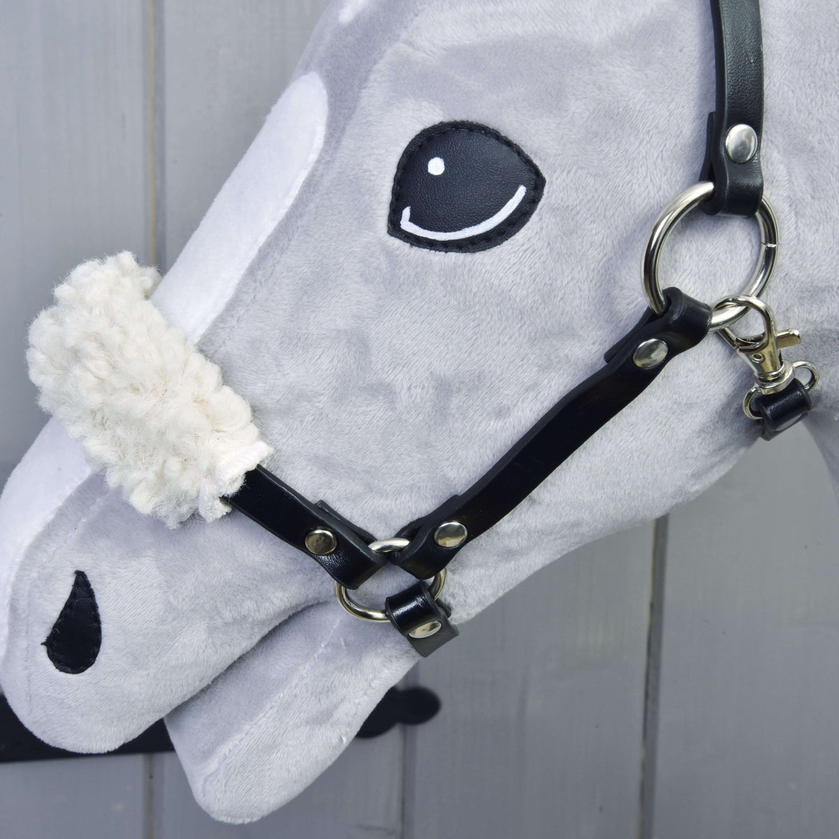 Close-up of the gray Set Basic Hobby Horse head by Hobby Horse LarDen, featuring a black bridle with reins and a white fuzzy noseband, set against a light wooden background.