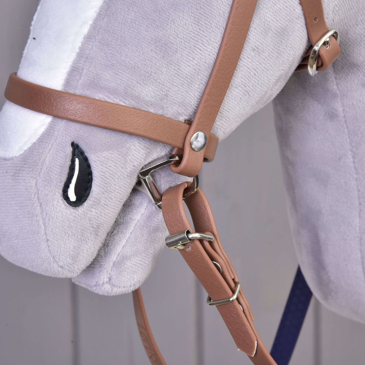 Close-up of a Hobby Horse LarDen plush horse head toy, featuring the Complete bridle with noseband Brown Purple and an embroidered black and white teardrop-shaped eye.