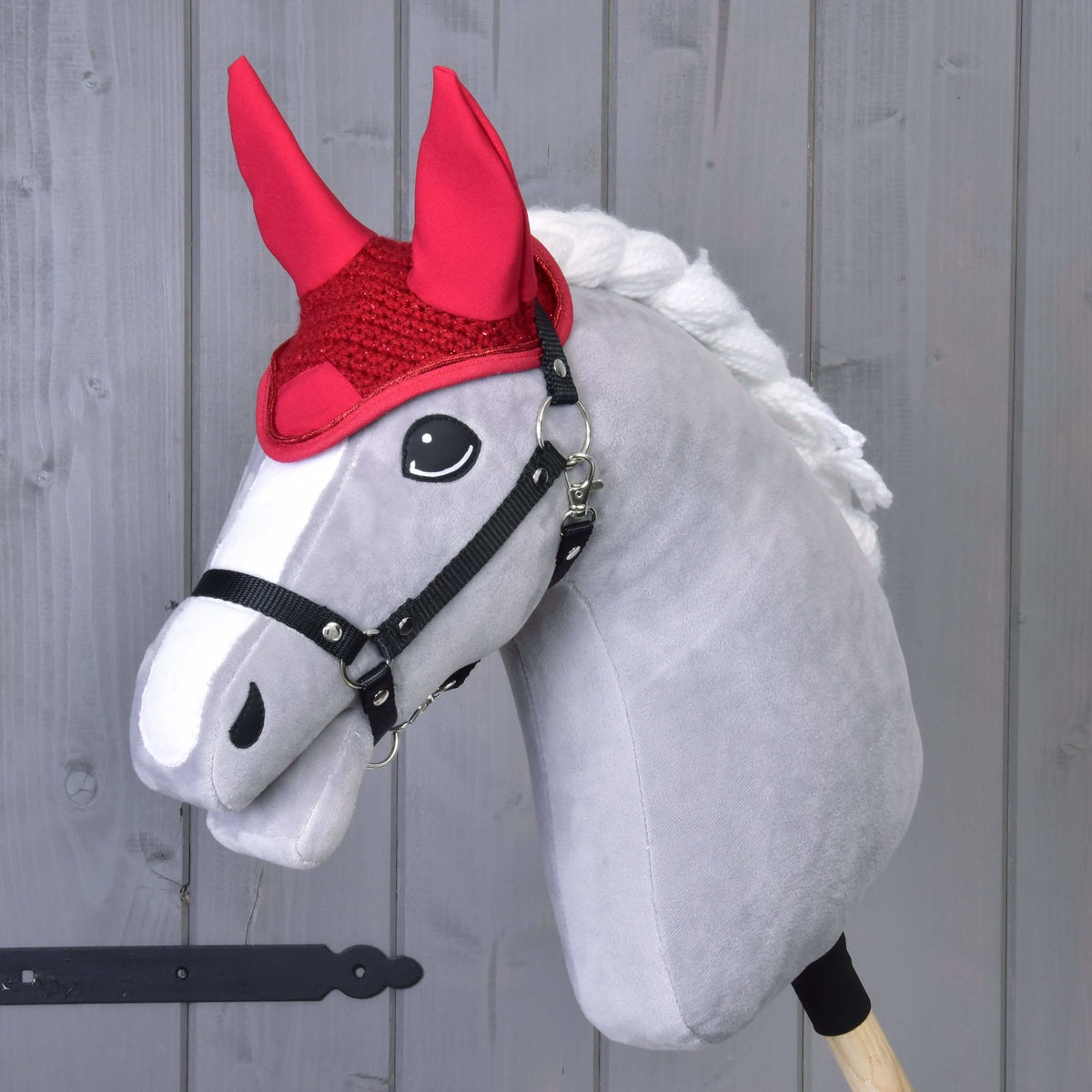 Grey Hobby Horse in a black halter wearing the red crocheted ear bonnet with tall fabric ears