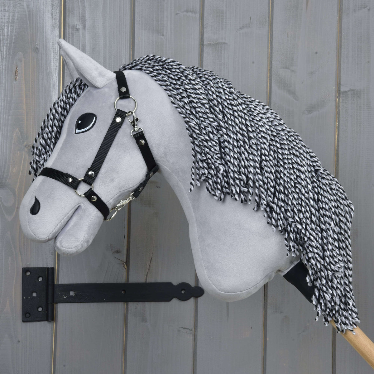 The Hobby Horse LarDen "Hobby Horse Caesar with Black Halter" features a gray plush head with a black and white yarn mane, black halter, and big cartoon eyes on a wooden stick—perfect for imaginative play.