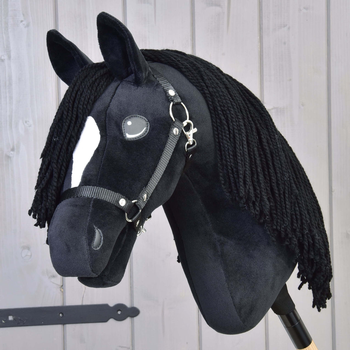The Hobby Horse LarDen "Hobby Horse Cloony with Black Halter" is a plush American Quarter Horse stallion with black fabric, a white facial patch, button eyes, black yarn mane, and bridle on a light wooden background.