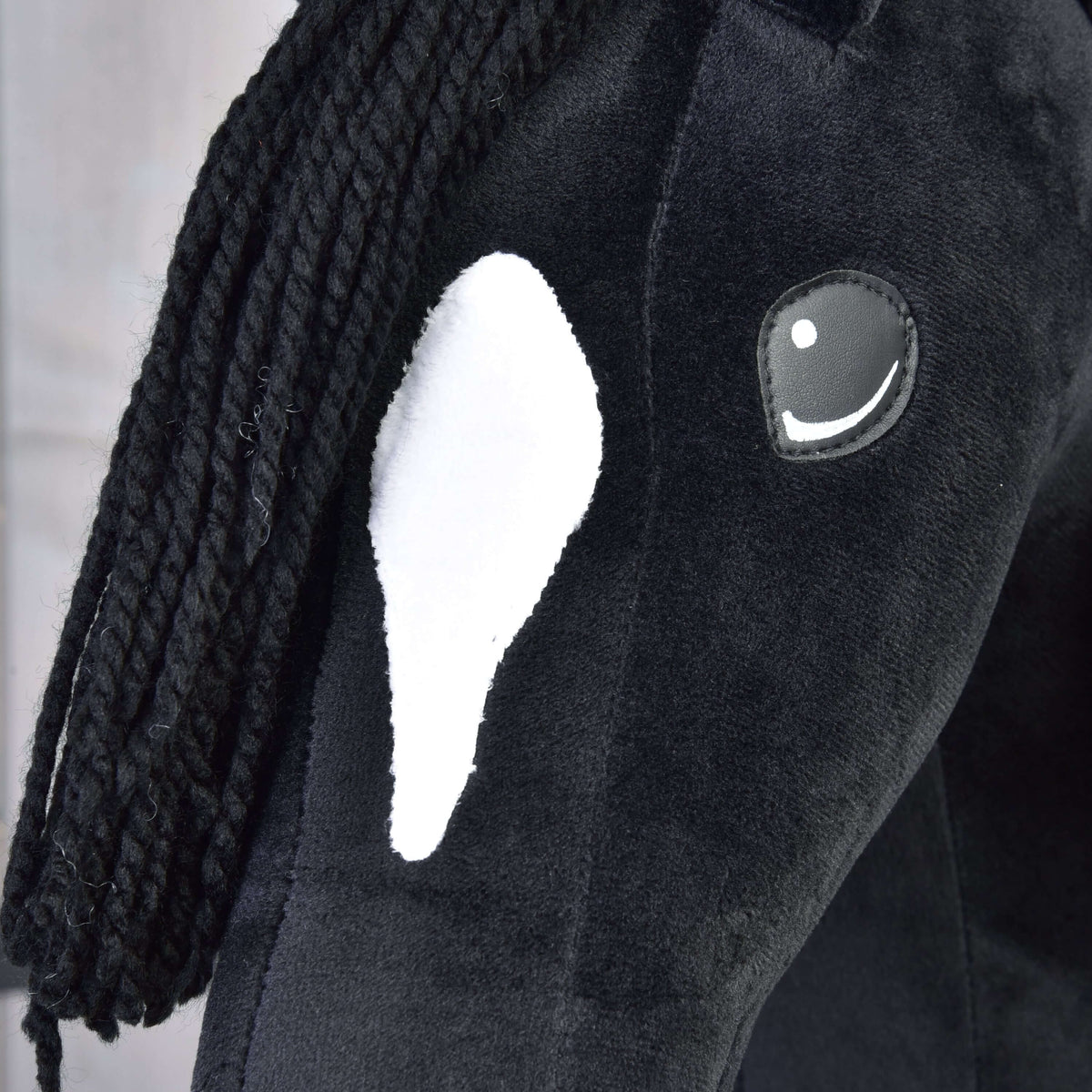 A close-up of Hobby Horse LarDen's Cloony with Black Halter, a black plush hobby horse with a white face patch, black yarn mane, and an embroidered eye with a white highlight.