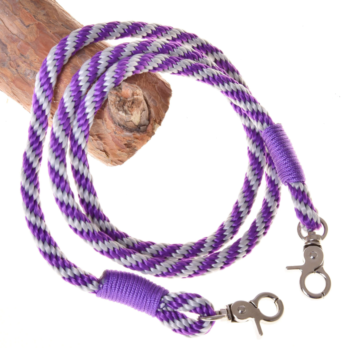 The Hobby Horse LarDen Set Start Purple includes a halter, cordeo, lead rope, and reins in coiled purple, white, and black with metal swivel clips—an ideal accessory set for hobby horse enthusiasts. Displayed on a wooden branch.