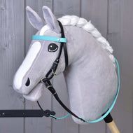 A gray plush hobby horse with a white mane and face markings features the Hobby Horse LarDen Complete bridle without noseband turquoise, black reins, and is mounted on a wooden stick in front of a gray wooden wall.