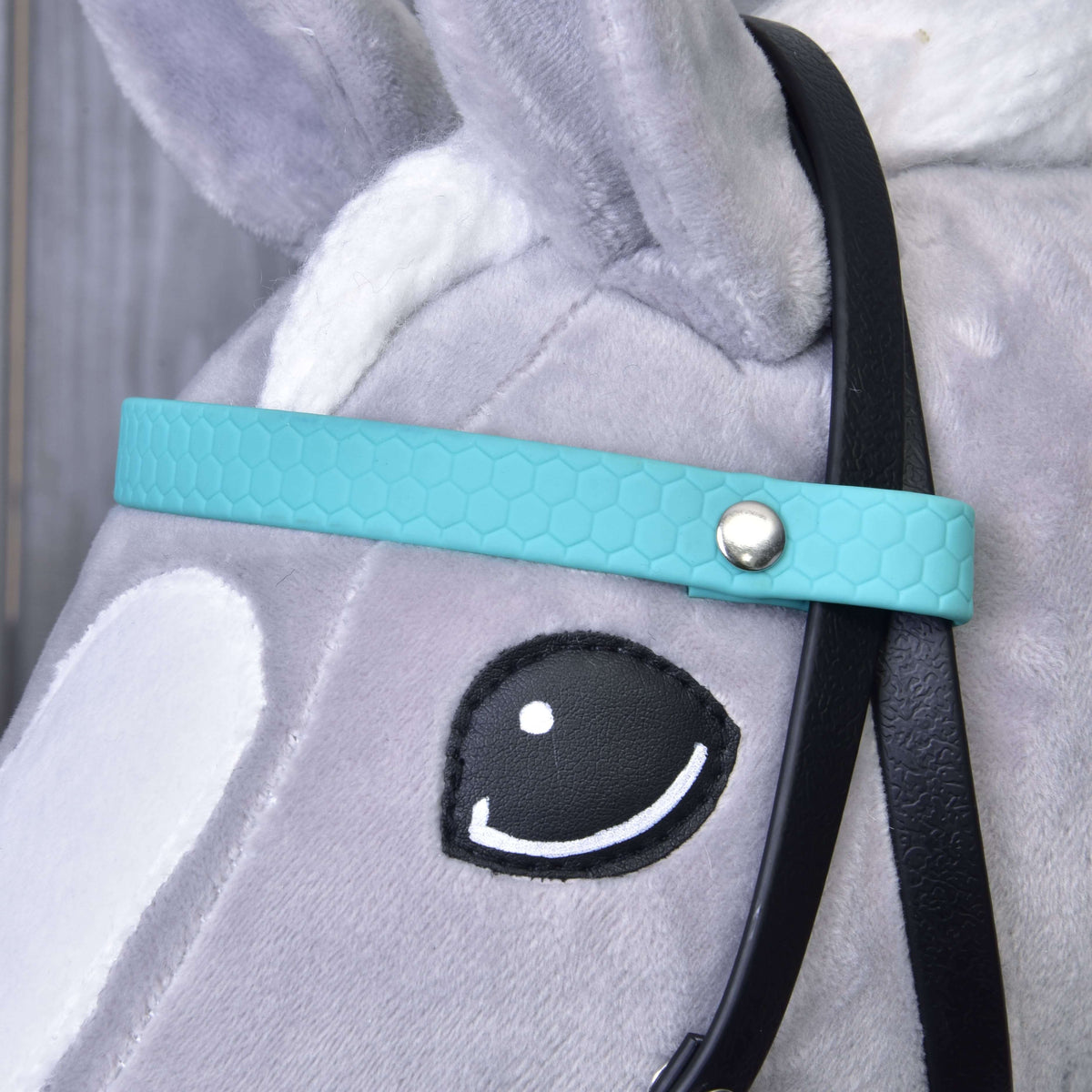Close-up of the turquoise browband with honeycomb texture and a silver rivet beside the eye of a grey Hobby Horse