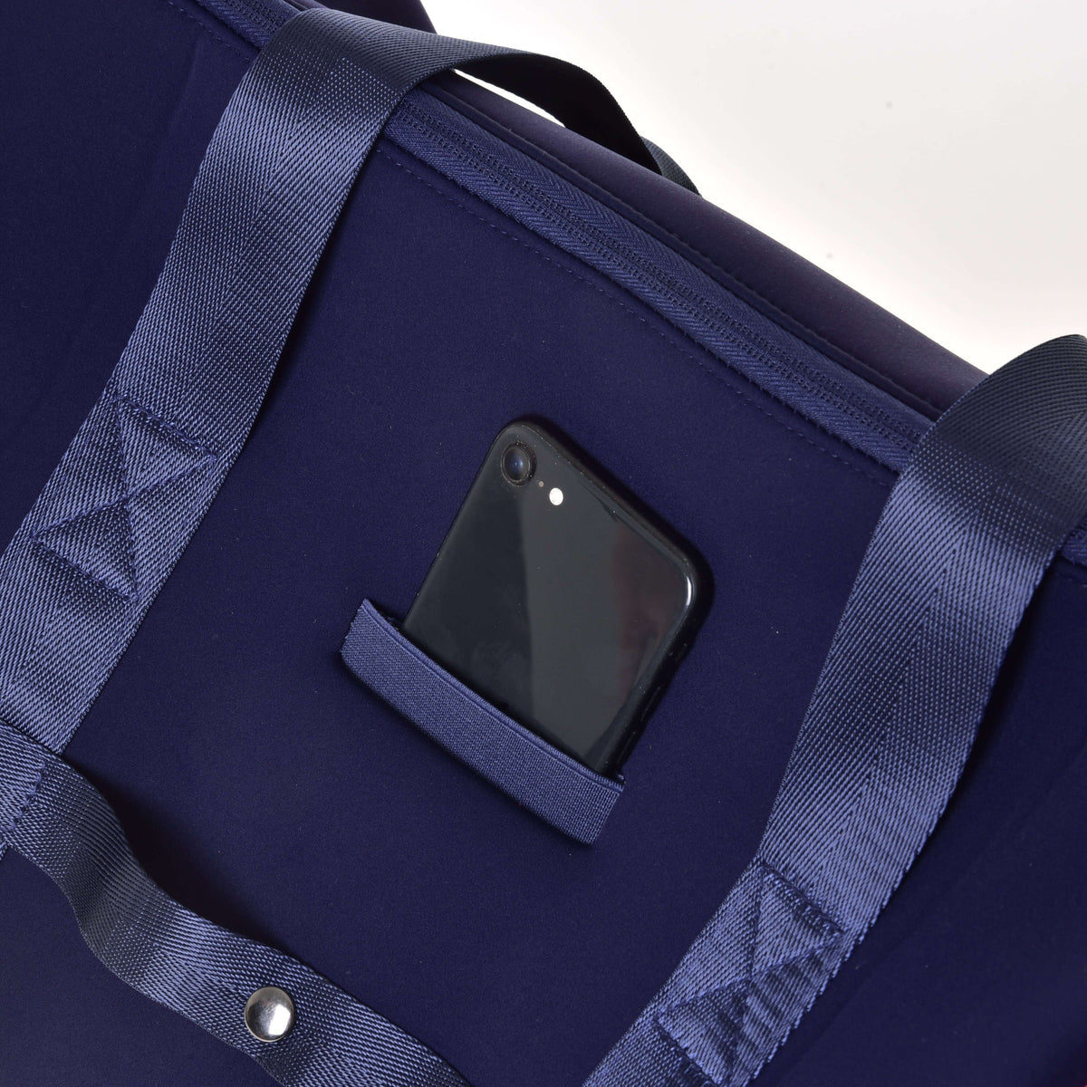 Black smartphone in the small slip pocket on the back of the navy Hobby Horse Sports bag, between the handles