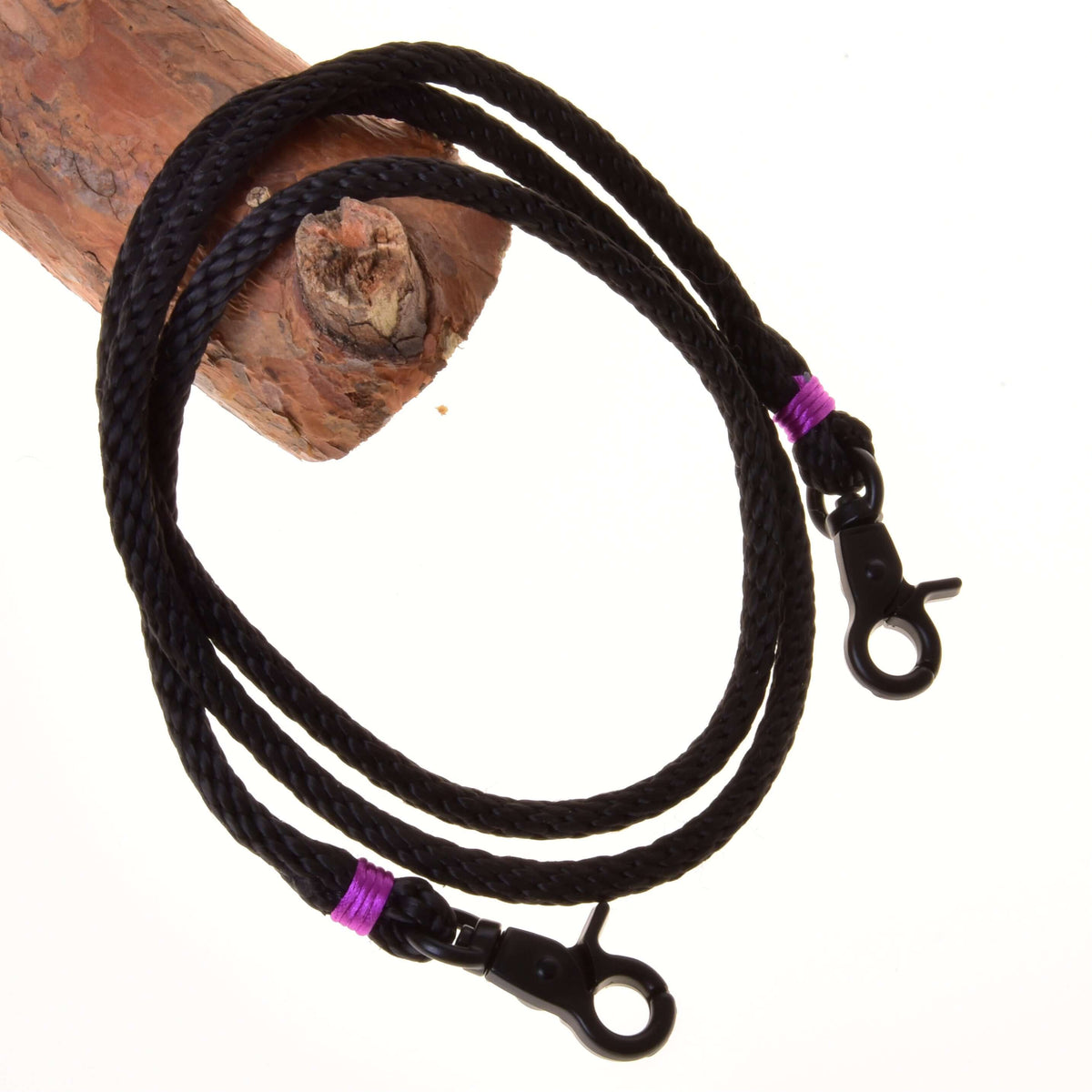 The Reins Violette from Hobby Horse LarDen are coiled black braided polypropylene reins with metal clips and purple wraps, shown draped over wood on a white background—ideal for handmade hobby horse reins.
