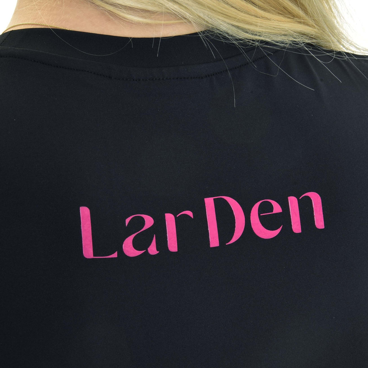 Detalje af den lyserøde LarDen-skrift på ryggen af en sort sportstrøje med rund hals og lyst hår over skulderen