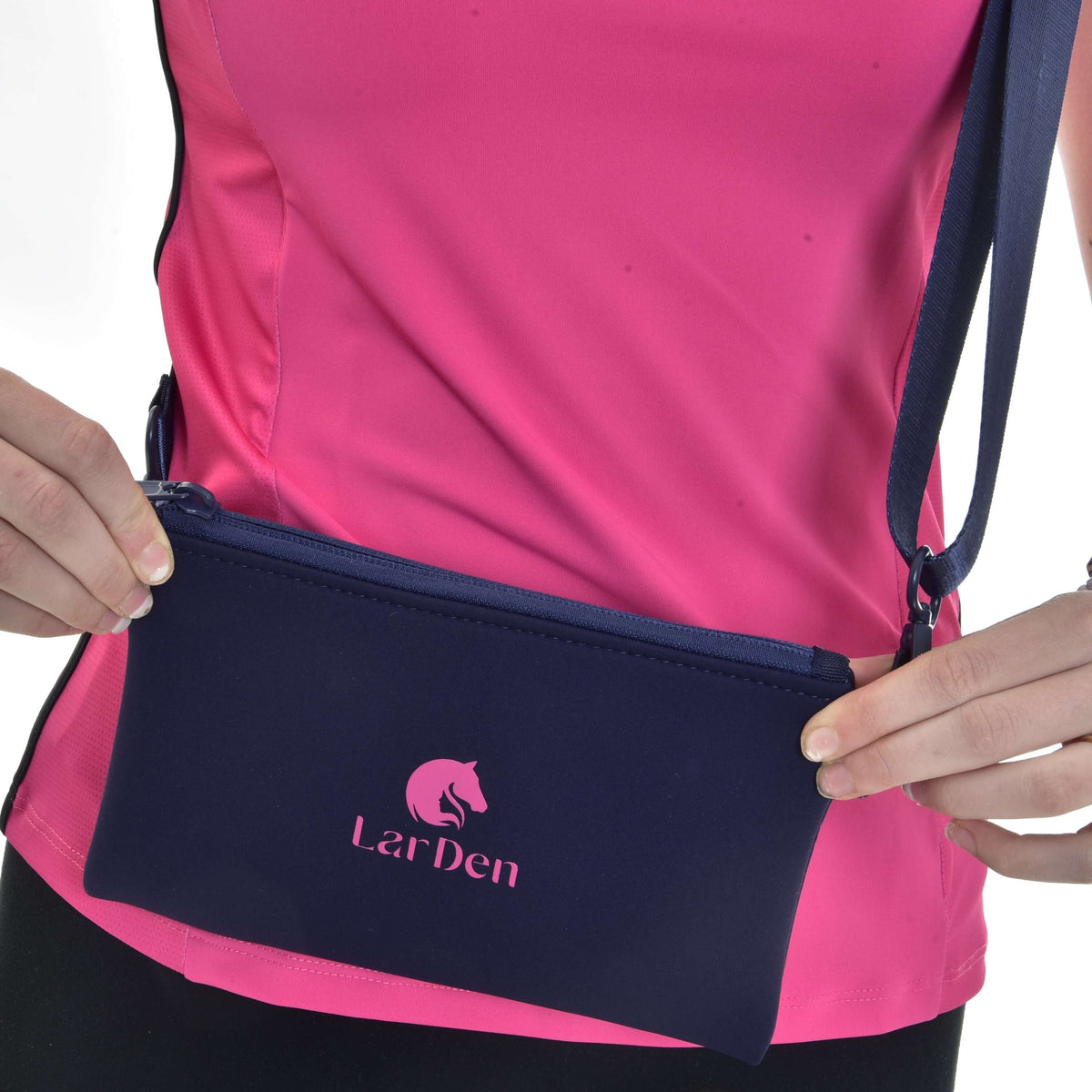 A person in a pink athletic top holds the Hobby Horse LarDen Cross body, a navy blue neoprene bag with an adjustable strap, zip closure, and the brand’s logo with horse graphic.