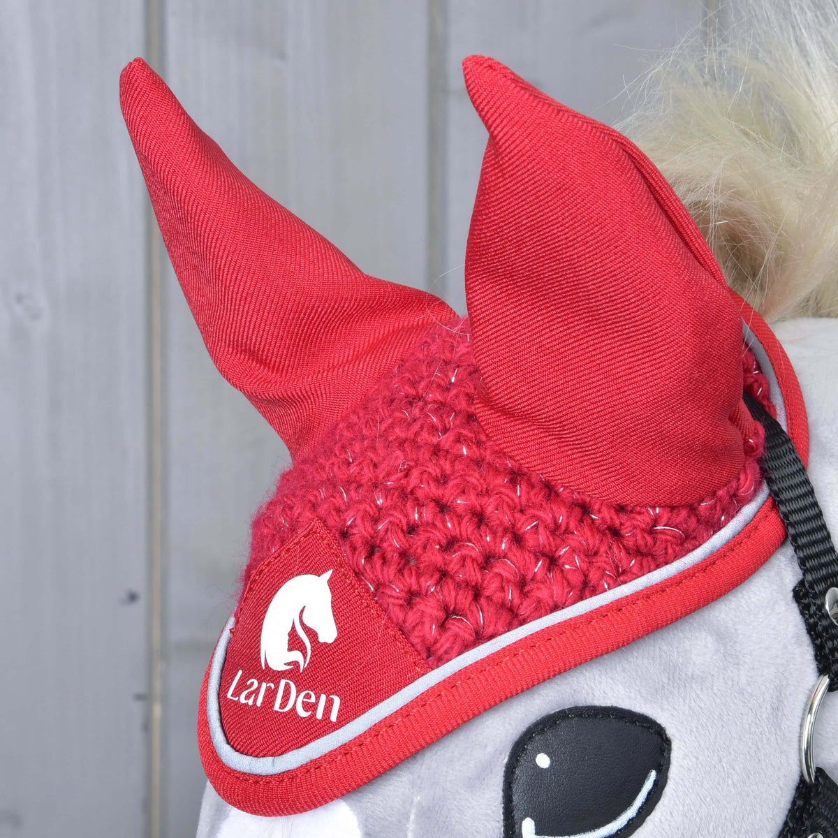 Close-up of the Ear bonnet crocheted Red Sport on a grey Hobby Horse: red fabric ears, sparkly crochet and LarDen logo