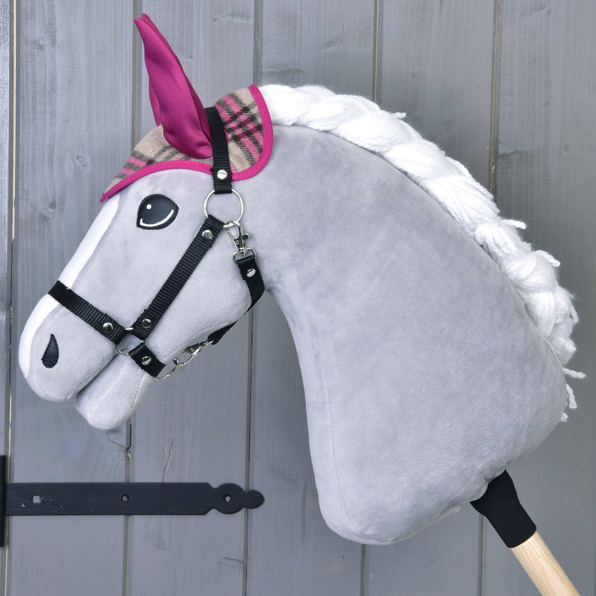 A gray plush Hobby Horse by LarDen with a white mane, pink and plaid ears, and black bridle stands on a wooden stick—perfect to pair with the Set Cube Pink for cozy playtime fun.