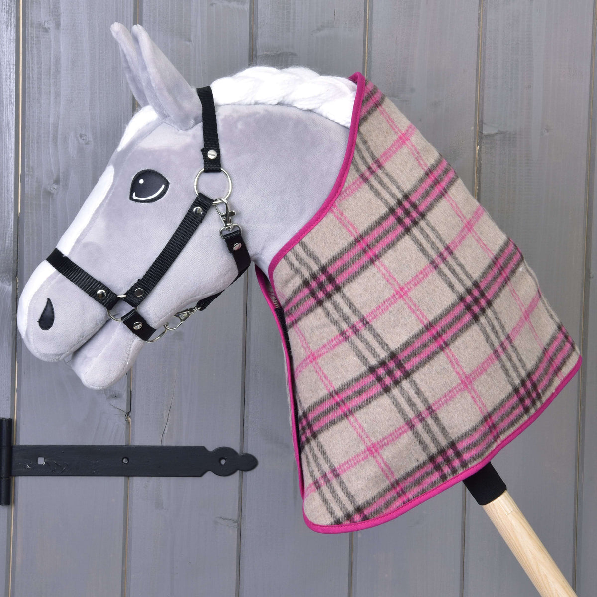 A gray plush Hobby Horse LarDen with a black harness and the Set Cube Pink plaid blanket set draped over its neck, set against a wooden background.