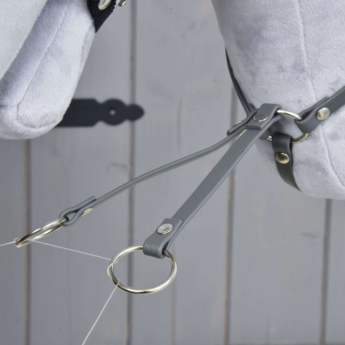 Close-up of the Martingale dark grey by Hobby Horse LarDen, featuring grey leather straps and a leatherette martingale with metal rings on a light grey stuffed horse head, displayed against a wooden background.