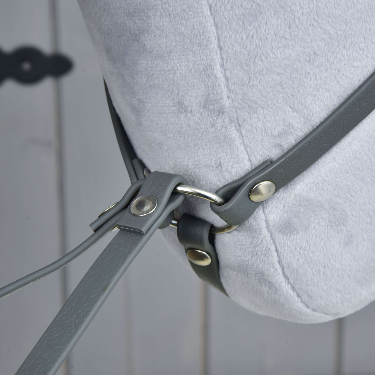 Close-up of the Martingale dark grey by Hobby Horse LarDen on a light grey plush horse head, featuring grey leather straps and metal rings against a blurred wooden background.