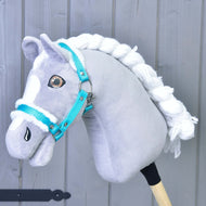 A gray and white hobby horse with a braided white mane wears the Hobby Horse LarDen "Halter turquoise with fur," the perfect accessory, set against a light gray wooden background.