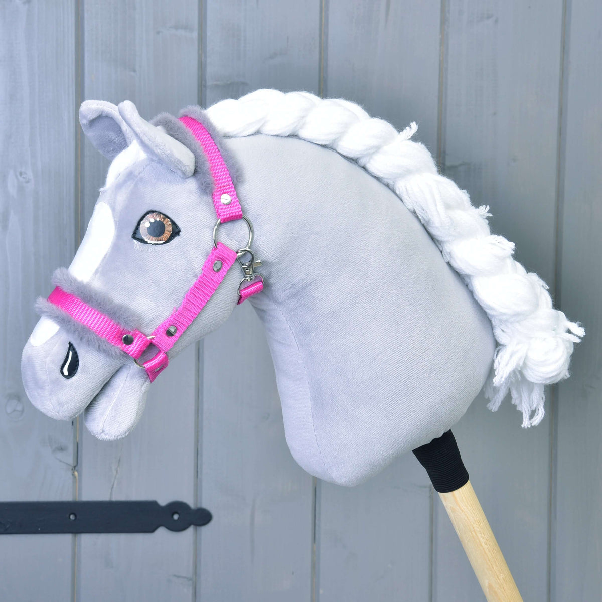 The Hobby Horse LarDen "Halter pink with fur" is shown on a gray hobby horse with a white yarn mane, white facial markings, and mounted on a wooden stick against a gray wooden background.