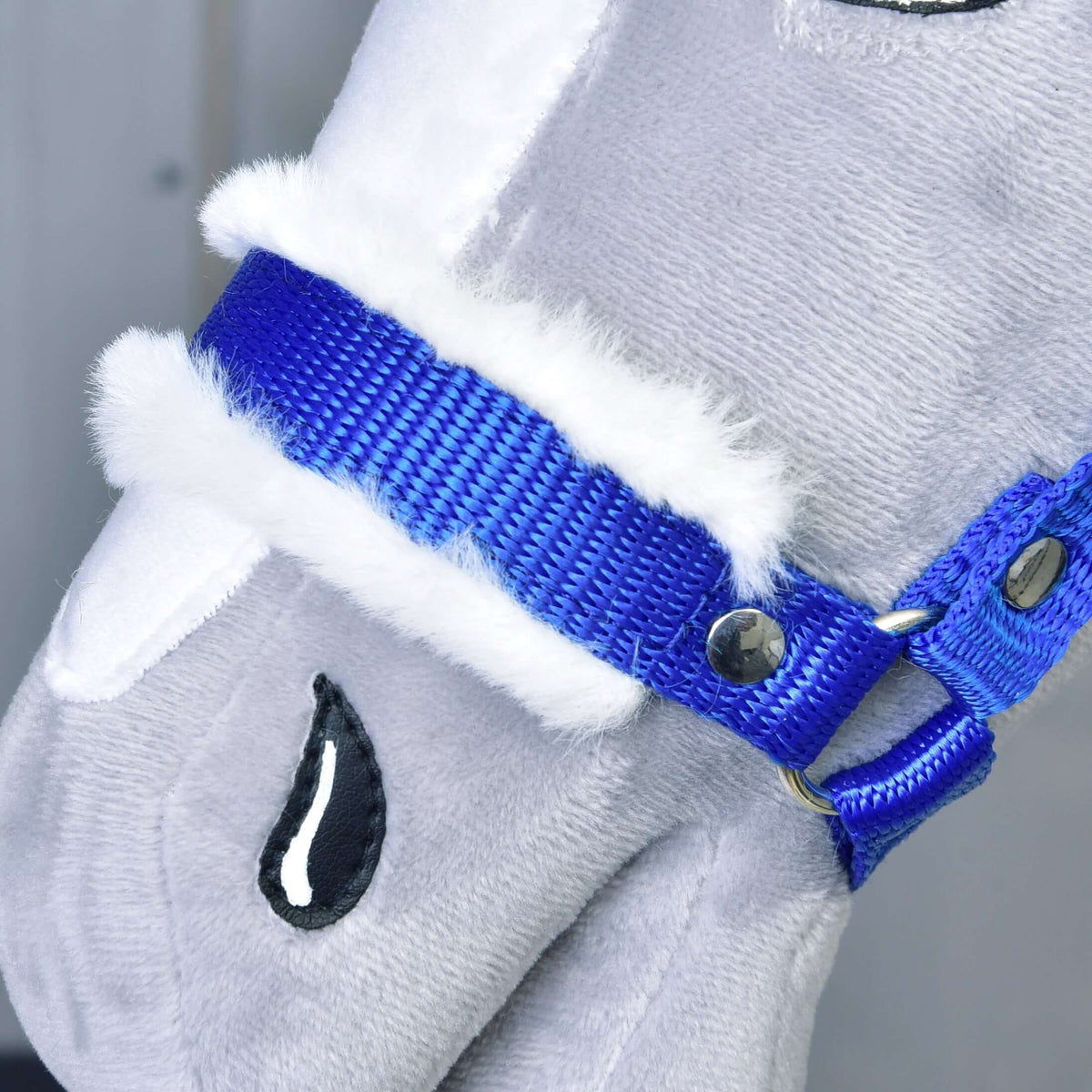 Close-up of a Hobby Horse LarDen plush toy horse’s face, showcasing the Halter blue with fur. Features include white faux fur trim, embroidered black eyes with teardrop detail on light gray fabric.