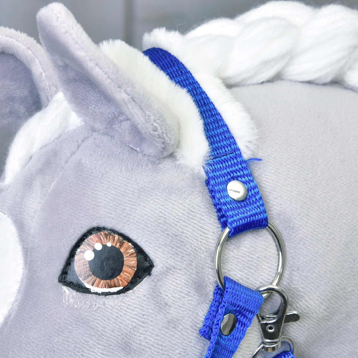 Close-up of a plush toy horse’s head with a white mane, wearing the Halter blue with fur by Hobby Horse LarDen. Features realistic embroidered eyes and soft gray fabric.