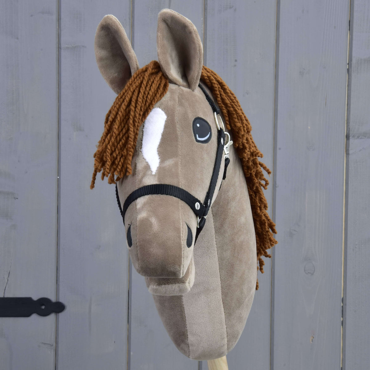 Hobby Horse LarDen's "Hobby Horse Oliver" is an Oldenburg stallion plush with brown fur, a white blaze, a brown yarn mane, black halter, and includes a free fur halter. Set against a gray wooden background.