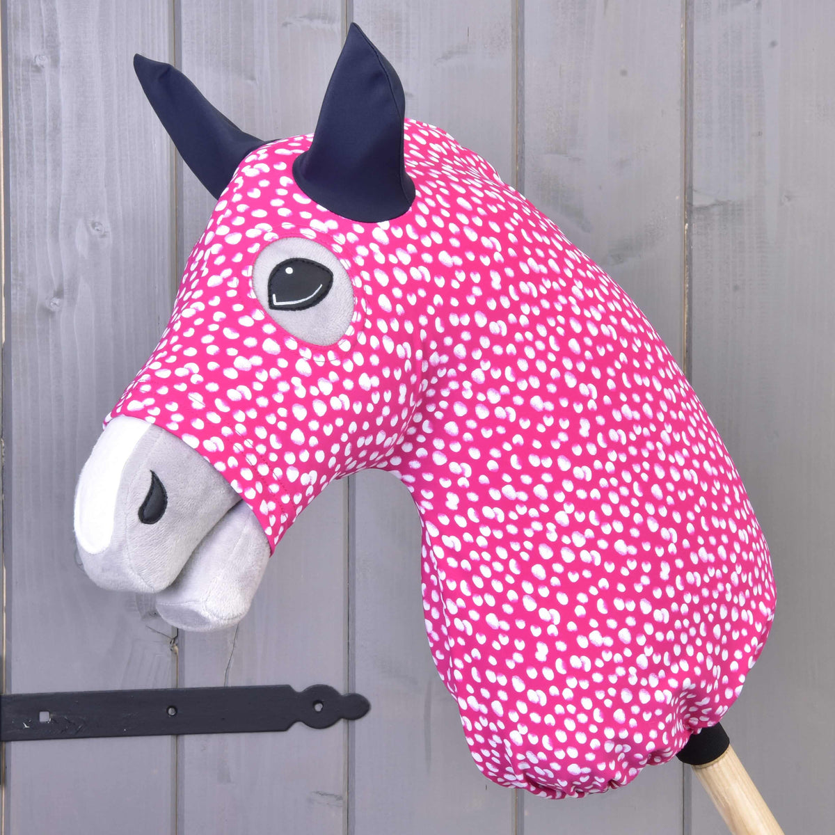 The Hobby Horse LarDen "Hobby Horse Protective suit Minie (Lycra)" is a pink hobby horse with white spots, grey snout, black ears, wooden stick handle, and features a washable Lycra cover for easy cleaning.