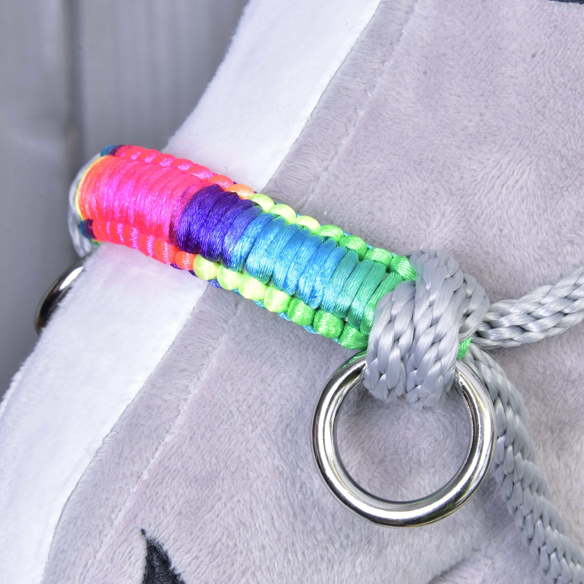 A close-up of a gray plush object with a rainbow strap on a shiny metal ring, fastened by the Rope halter Manhattan from Hobby Horse LarDen—an ideal and unique accessory for your hobby horse.