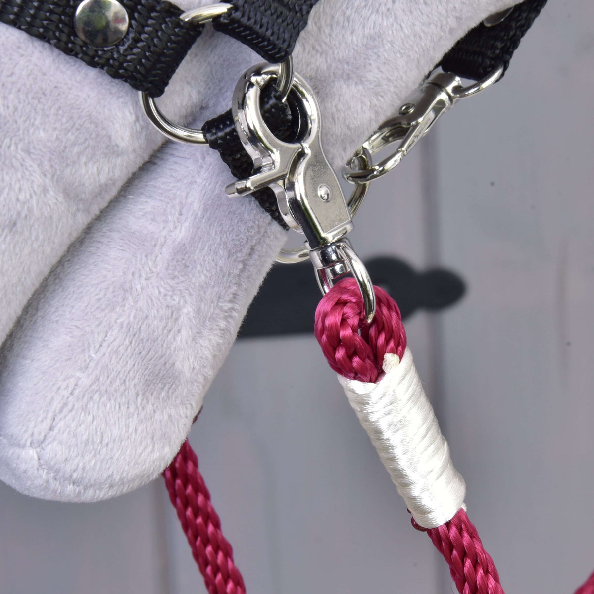 Close-up of the metal clasp attaching a braided pink polypropylene rope with white tape to soft light gray fabric and a black strap, part of the handmade Reins Czi-czi by Hobby Horse LarDen.