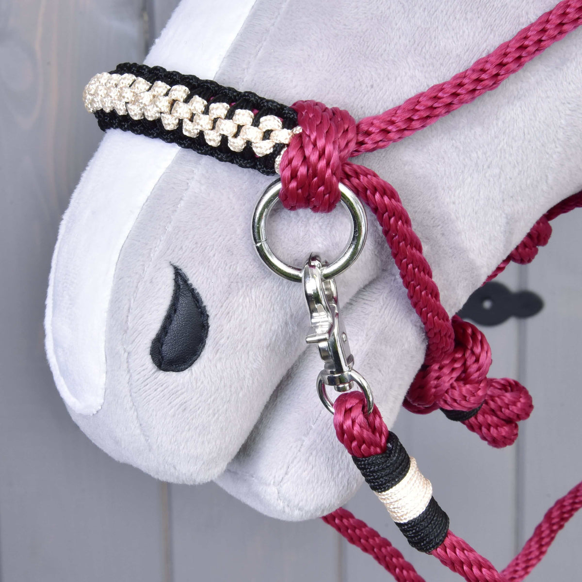 Close-up of a Hobby Horse LarDen head wearing the Rope set Burgundy, featuring a red and black rope halter with silver clip, braided band, simple stitched black eye, soft gray nose, and matching reins.