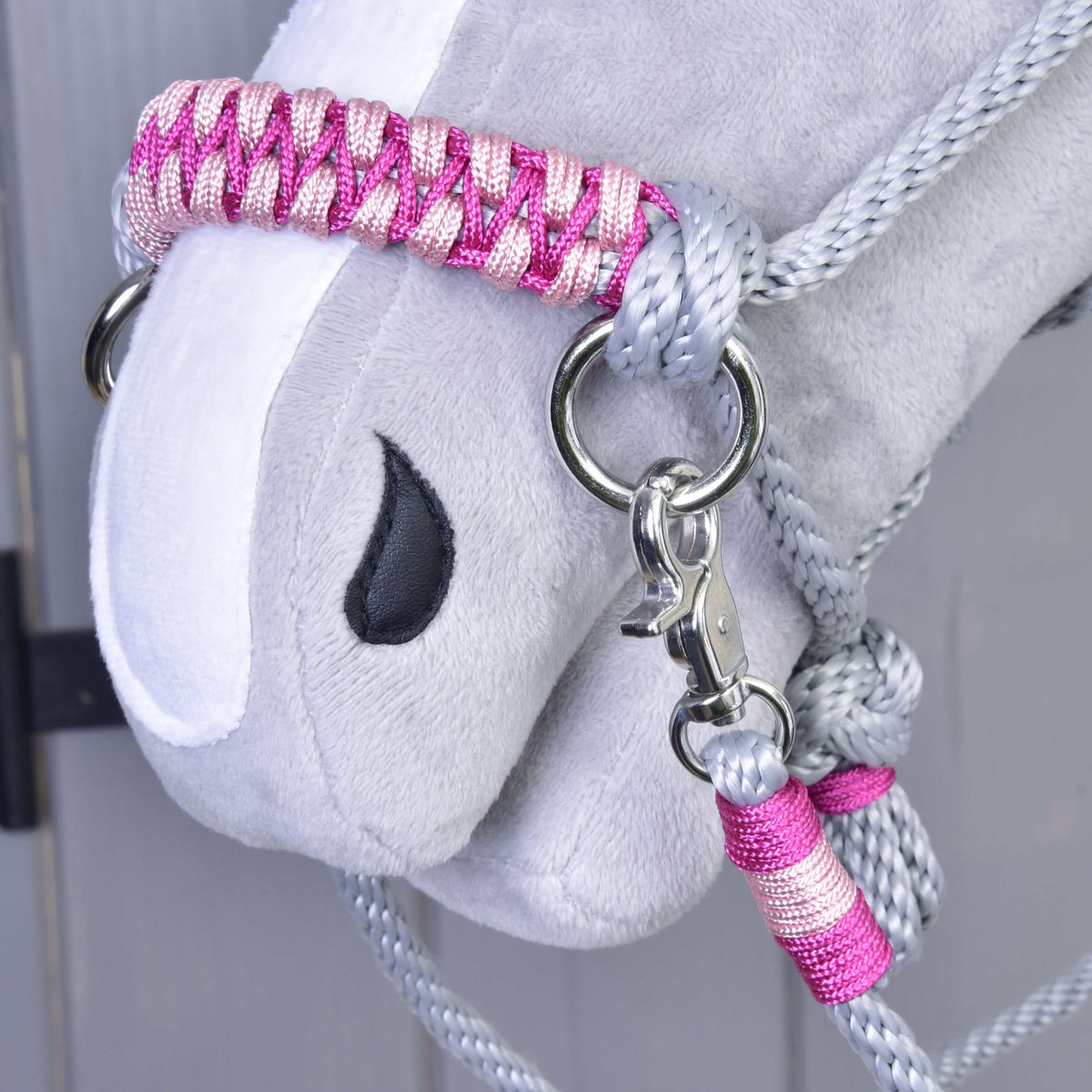 Close-up of Hobby Horse LarDen’s gray plush head with the Rope set Rosie: a pink and silver braided halter and lead rope, black embroidered eye, metal clasp, against a light wooden background.